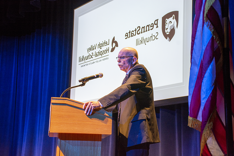 Bill Rowan delivers his presentation in front of a projected image of Penn State Schuylkill and Lehigh Valley Hospital - Schuylkill logos